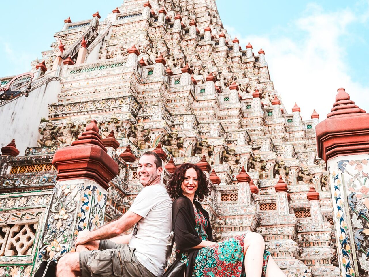 UnViaggioPerDue: Daniele e Flavia sono seduti fianco a fianco, sorridendo di fronte alla struttura del tempio riccamente decorata di Wat Arun - il Tempio dell'Alba - con un cielo luminoso sullo sfondo.