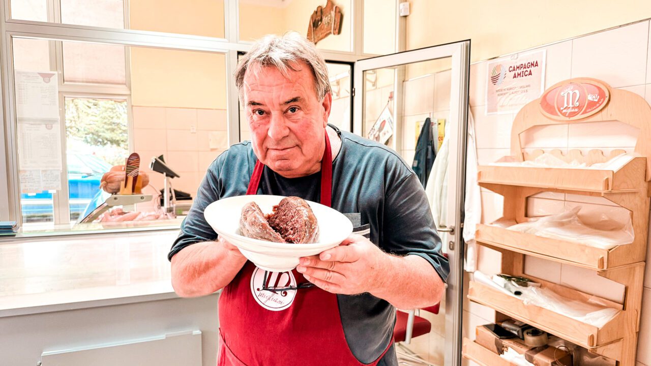 UnViaggioPerDue: un uomo in grembiule tiene in mano un piatto con la salama da sugo dell'Azienda Agricola Migliari, uno dei sapori autentici della provincia ferrarese.