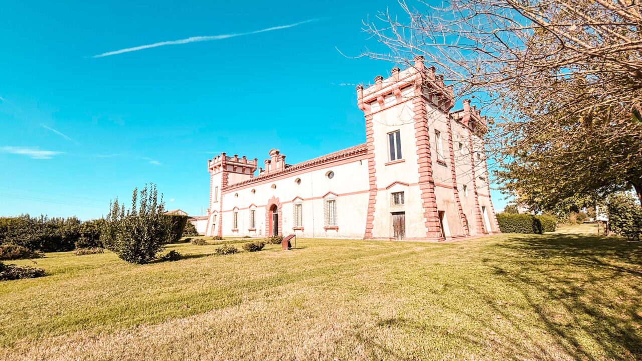 UnViaggioPerDue: in mezzo a un prato erboso tentacolare, sotto un cielo azzurro e terso, la Delizia del Verginese emerge come un castello rosa e bianco. Alberi maestosi e cespugli rigogliosi circondano amorevolmente questa incantevole struttura.